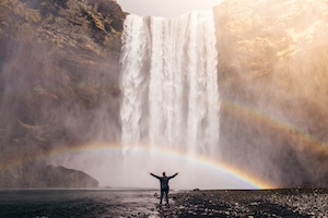 большой водопад, высокая отвесная скала, радуга, человек на фоне водопада 