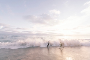 люди бегут по пляжу во время заката мимо волн и морской пены 