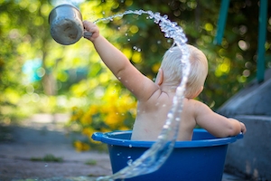 ребенок в синем тазике выливает воду из кружки 