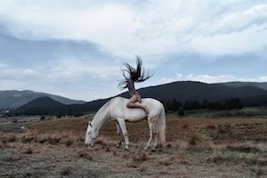 Молодая женщина на белом коне на фоне гор 