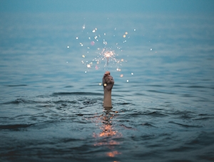 человек держит зажженный бенгальский фонарь посреди воды 