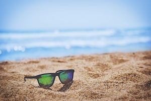 солнечные очки лежат на песке на пляже, прибрежная полоса, голубое море 