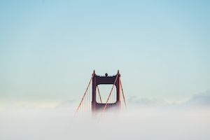 Часть конструкции красного моста над облаками, голубое небо 