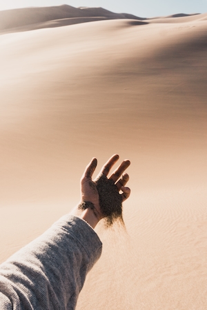 песок сыплется из руки человека на фоне песчаной дюны 