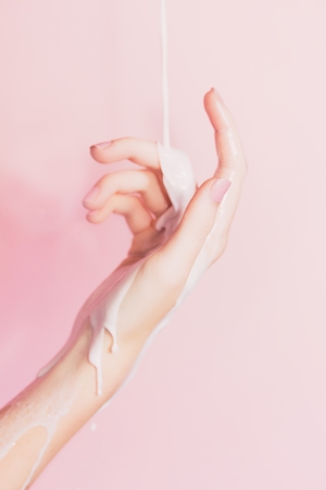Молоко течет по руке на розовом фоне 