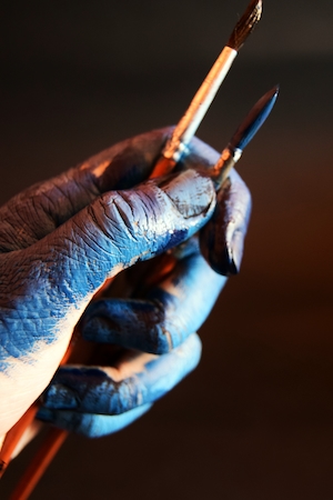 художник держит кисти испачканными в синей краске руками 