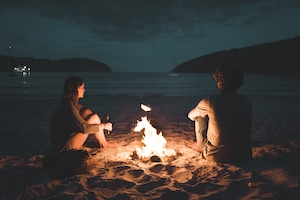 пара сидит у костра на пляже ночью