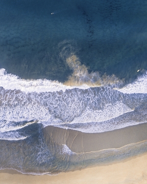 Песок высасывается из задней части волны, в то время как серферы дрейфуют в синеве, песчаный пляж, море, небо, голубая вода 