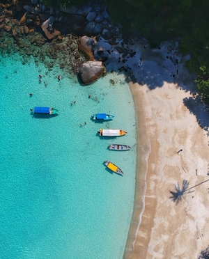 пляж со скалами, белый песок, голубая вода, лодки, фото сверху 