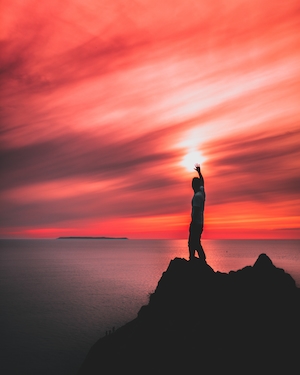 человек держит солнце во время красного восхода, силуэт скал и облака 