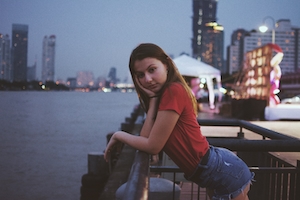 девушка позирует на камеру на фоне набережной вечернего города 
