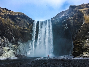 большой водопад, высокая отвесная скала, человек на фоне водопада 