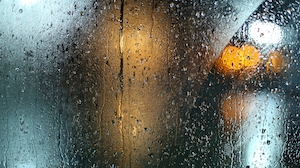 капли дождя на стекле, размытое разноцветное изображение за запотевшим окном 