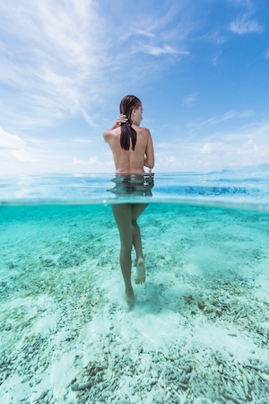 девушка по пояс в прозрачной бирюзовой воде, фото со спины 