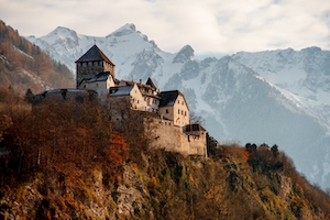 Замок Вадуц в окружении осеннего леса на фоне снежных гор 