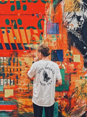 человек в белой футболке стоит на фоне разноцветного граффити 