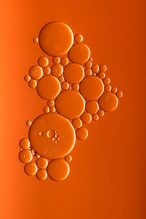 масло в воде с капелькой жидкости для мытья посуды, капли масла на оранжевом фоне 