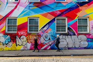 люди идут на фоне стены дома с ярким разноцветным граффити 