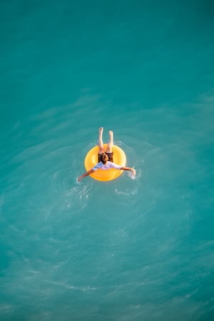 Мальчик, плавающий в море в желтом надувном круге посреди бирюзового моря 