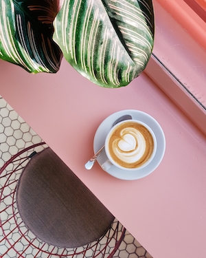 Чашка кофе с рисунком на розовом столе, растение 