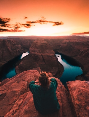 Изгиб подковы, красные скалы каньона, небо на закате, человек смотрит на ущелье 