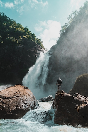 большой водопад, высокая отвесная скала, человек на фоне водопада 