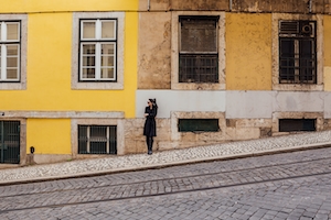 Человек ожидает на улице с трамвайными путями на фоне желтых зданий 