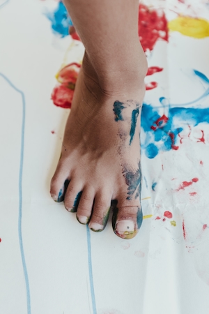 ребенок делает отпечаток своей ноги синей краской 