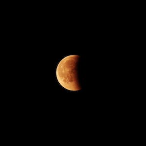 лунное затмение, изображение оранжевой луны на черном фоне 