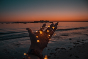 гирлянда в руке человека на фоне моря во время заката 