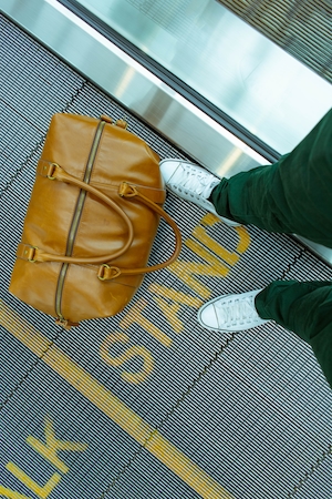 Стоя на движущейся дорожке в аэропорту с багажом, желтая сумка