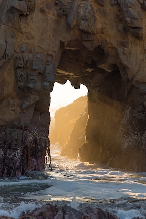 большая каменная арка на песчаном пляже, солнце во время заката 