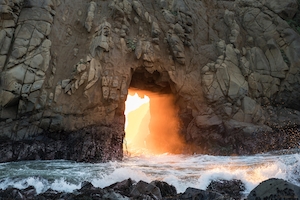большая каменная арка на песчаном пляже, солнце во время заката 