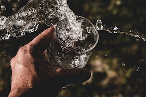 всплеск воды, воды выливается из стакана в руке человека 
