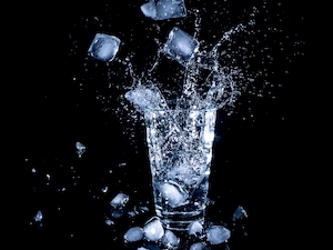 Кубики льда падают в стакан с водой, всплеск воды 