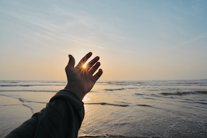 рука человека на фоне закатного неба над морем 