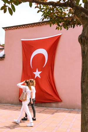 туристы гуляют рядом с флагом Турции на стене 