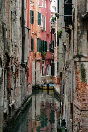 Широкая лодка, покоящаяся в узком канале Венеции, окруженная множеством окон.