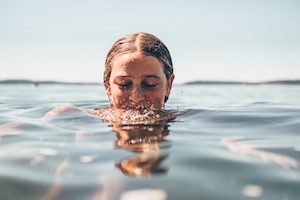 Девочка-подросток в океане, ее голова частично высунута из воды. 