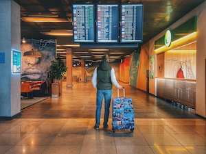 Человек с ярким чемоданом смотрит на табло в аэропорту