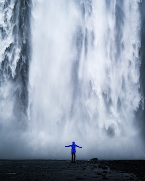 Водопад Скогафосс в Исландии, большой водопад, высокая отвесная скала, человек на фоне водопада 