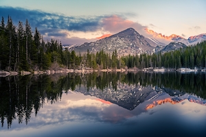 Отражение Медвежьего озера в национальном парке Роки Маунтин. Горное озеро, отражение неба и гор в воде, лес у озера и гор во время заката 
