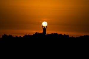 Силуэт человека на фоне заката, красочное солнце и небо, человек держит солнце в руках 