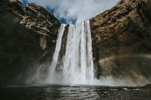 отвесный водопад посреди высоких отвесных скал, бассейн, радуга 