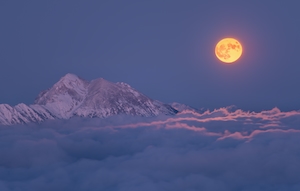 Большая полная луна поднимается над туманным горным пейзажем. 
