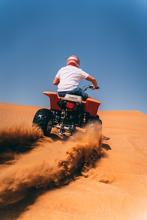 Человек едет по песку в пустыне на квадроцикле