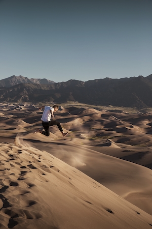 песчаные дюны, барханы, каньон, отвесные скалы, человек в прыжке 