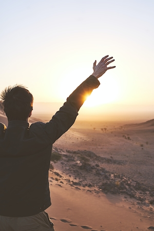 Мужчина с поднятыми руками в пустыне на восходе солнца, силуэт человека на фоне заката, красочное солнце и небо