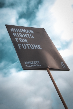Плакат "Права человека во имя будущего" от Amnesty International, черный плакат на фоне неба 
