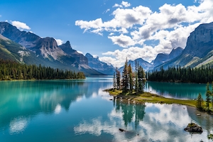 Прекрасная фотография знаменитого острова Духов на озере Малинь в национальном парке Джаспер в самом сердце Канадских Скалистых гор. Горное озеро, отражение неба и гор в воде, лес у озера и гор